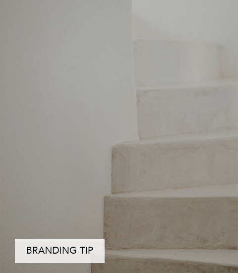 Eine schlichte, helle Steintreppe mit sanft gerundeten Kanten, die minimalistisch in einen weißen Putzwandhintergrund übergeht.